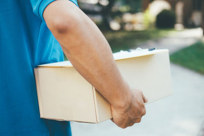 Midsection of delivery man with box walking outdoors