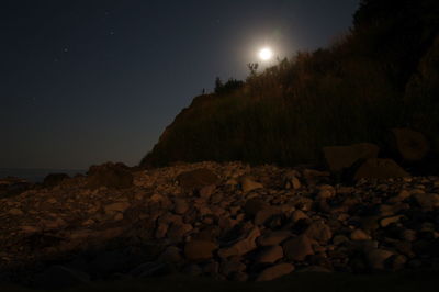 Rocks on beach against sky at night