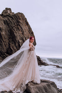 Woman standing on rock by sea against sky