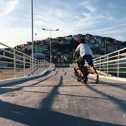 Rear view of boys playing with push scooter on bridge in city against sky