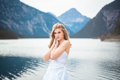 Portrait of beautiful woman standing by lake against mountains