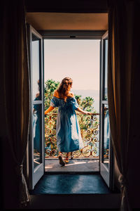 Side view of woman looking through window, standing on the balcony, summer days, vacation, dress