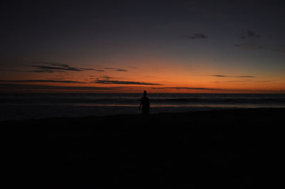 Silhouette man standing on beach against sky during sunset