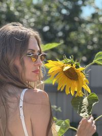 Portrait of young woman wearing sunglasses while standing against tree