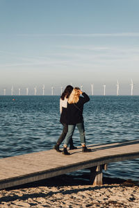 Friends walking on pier over sea against sky