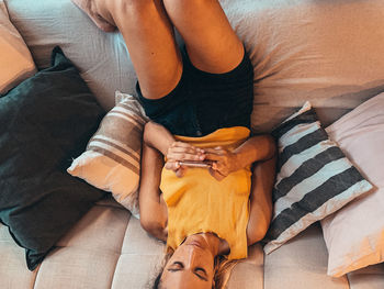 High angle view of woman using smart phone while relaxing on sofa at home