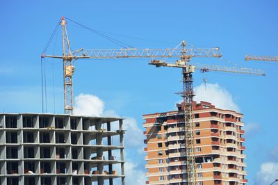 Low angle view of crane by building against sky