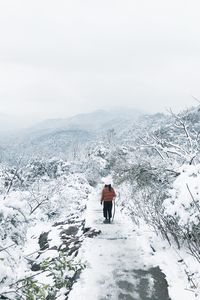 Rear view of man walking on snow covered mountain against sky