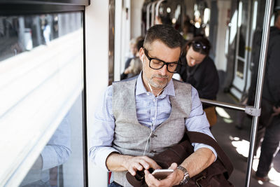 Businessman with smartphone and earphones travelling in tram