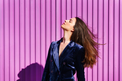 Woman looking away while standing against pink wall