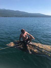 High angle view of shirtless mature man sitting on wood in lake