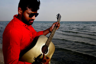 Young man playing guitar against sea