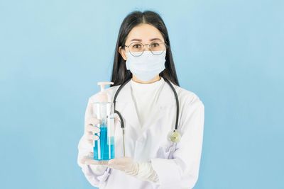 Portrait of doctor holding hand sanitizer against blue background