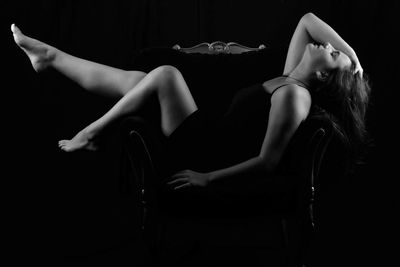 Full length of sensuous woman reclining on chair against black background