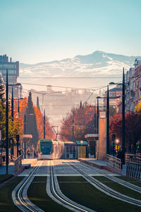 Contemporary tram driving on tracks near apartment buildings and deciduous trees against snowy mountain peak on autumn day in granada, spain