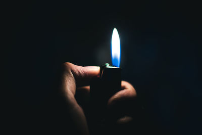 Cropped hand of person igniting cigarette lighter against black background