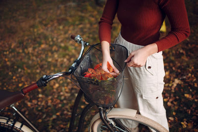 Midsection of woman with bicycle on autumn leaves