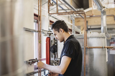 Side view of auto mechanic student analyzing machinery in workshop