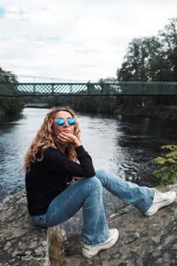 Side view of young woman sitting against lake