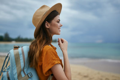 Young woman looking away while standing on beach against sky