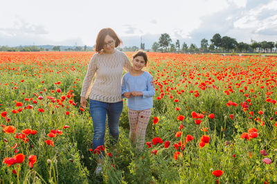 Mother and daughter walking in the poppy field next on a sunny day