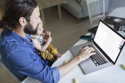 High angle view of mid adult man with baby boys working on laptop at home