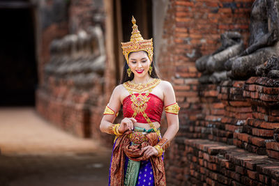 Young woman in traditional clothing standing against built structure
