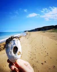Person holding sand on beach against sky