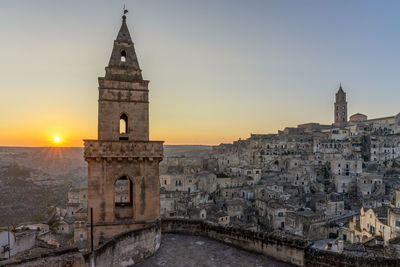 Church tower and historic buildings on a hill against sky during sunrise in the town matera in italy