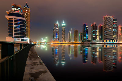 Illuminated buildings by river against sky in city at night