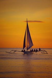 Sailboat sailing in sea against orange sky