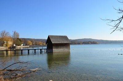 Built structure by lake against clear blue sky