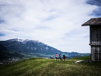 Rear view of man and women walking on grassy hill against cloudy sky