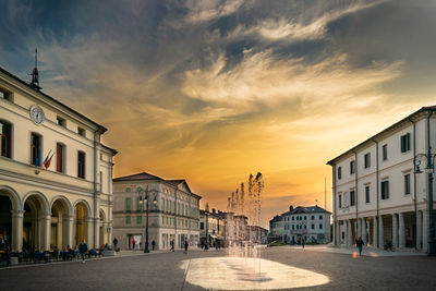 Street amidst buildings against sky during sunset