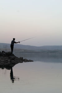 Man fishing in lake against sky