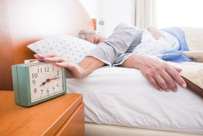 Senior woman stopping alarm clock while sleeping on bed at home