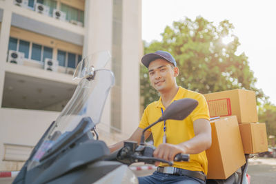 Portrait of smiling delivery man sitting with parcels on scooter