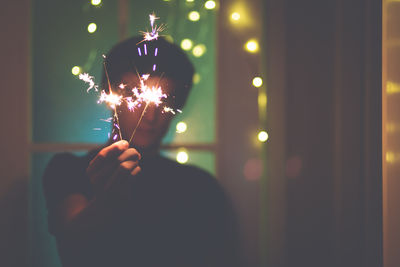 Teenage boy burning sparkler while standing at doorway