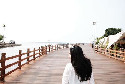 Rear view of young woman standing by sea against clear sky