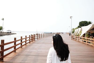 Rear view of woman with long hair walking on promenade against sky