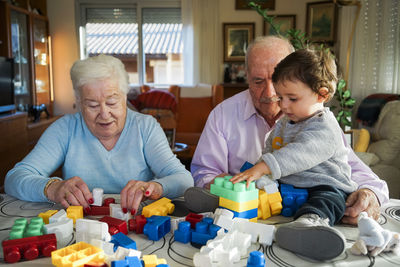 Great-grandparents and baby girl playing together with plastic building bricks at home