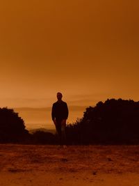 Silhouette man standing on field against fire red sky