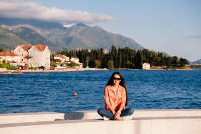 Portrait of smiling woman sitting by mountains against sky