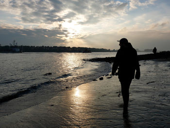 Silhouette people on calm beach at sunset