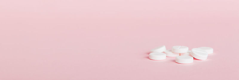 Close-up of pills spilling from bottle against pink background