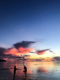 Silhouette people on beach against sky during sunset