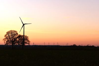 Silhouette of wind turbines on field during sunset