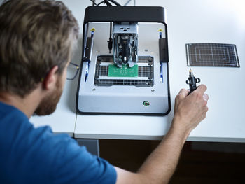 Technician looking at milling machine cutting circuit board in electronic laboratory