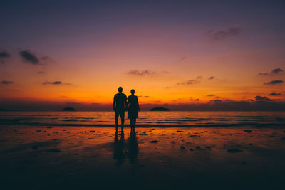 Silhouette couple standing on sea shore at beach against sky during sunset