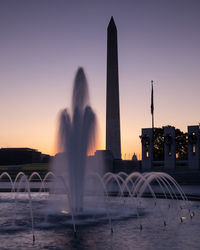 Fountain in city against sky during sunset